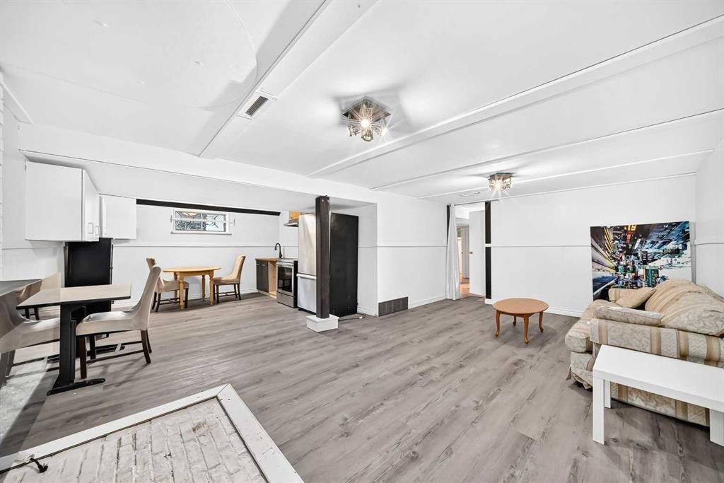 Bright open living room with white walls, gray wood floors, sofa, dining area, and kitchen visible.