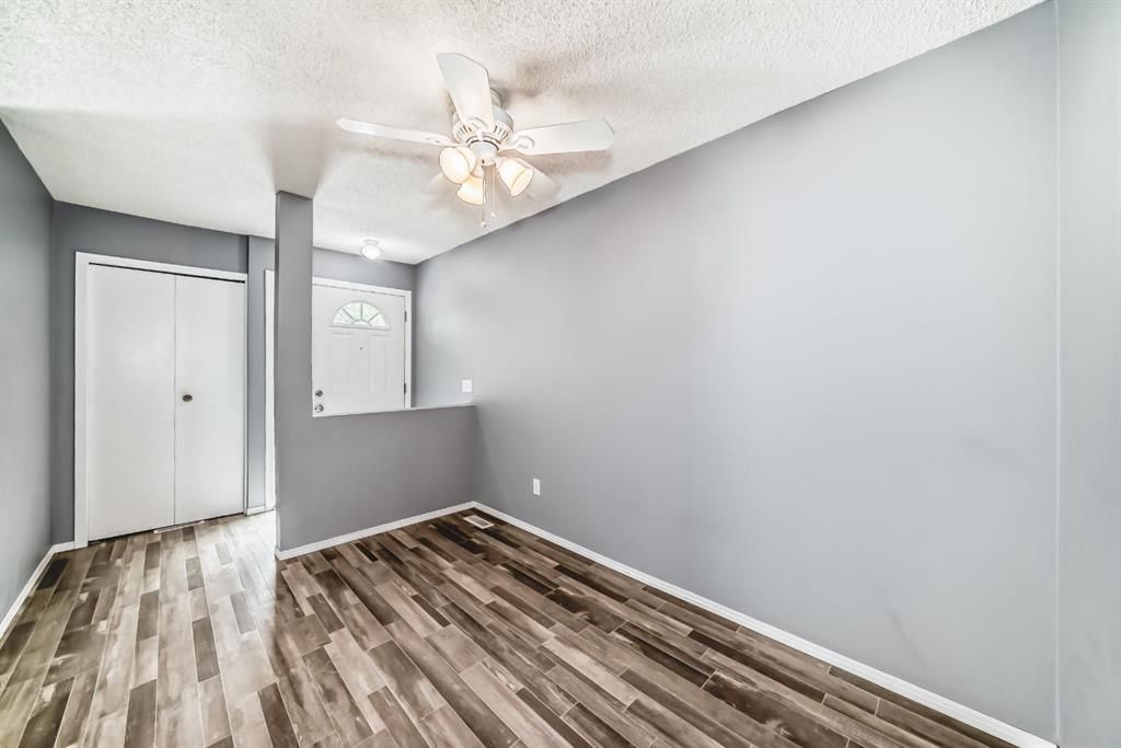 Empty gray bedroom with wood-look flooring, ceiling fan, and closet doors.
