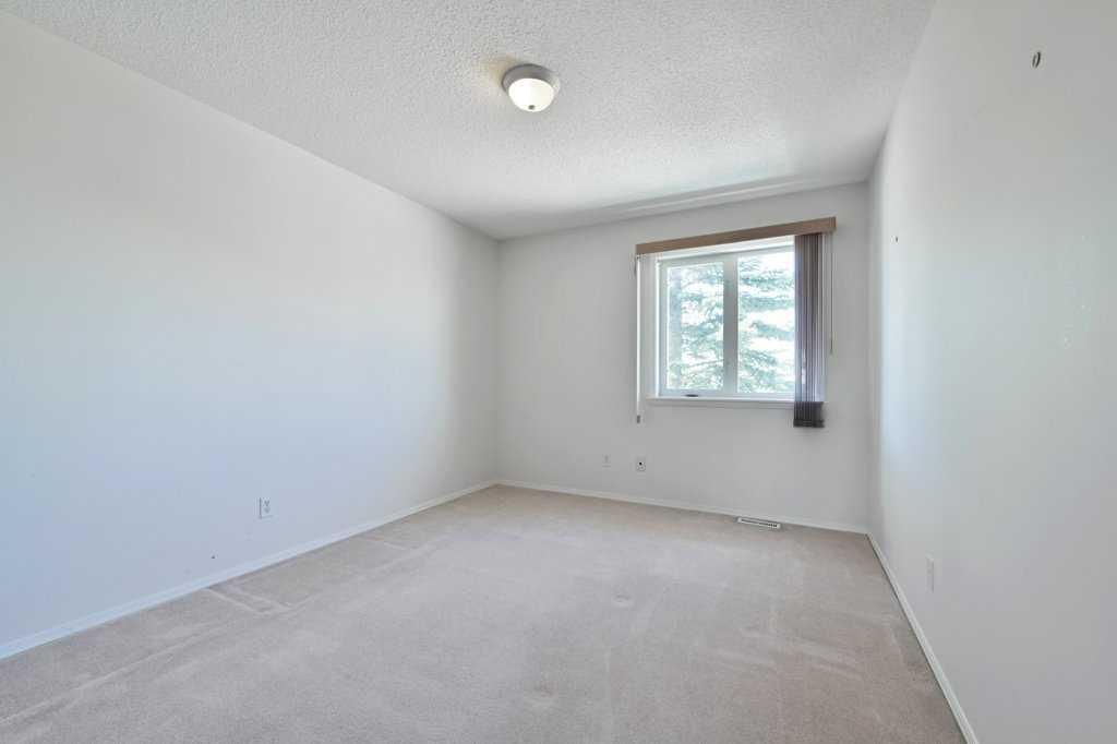 Empty white bedroom with beige carpet and a window letting in daylight