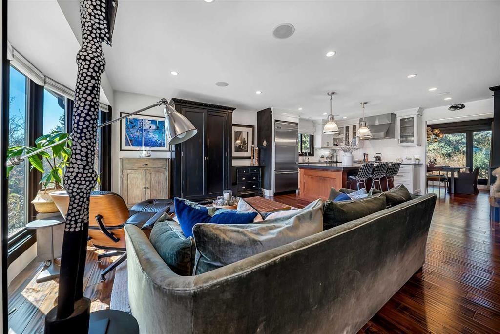 Spacious modern living room with dark sofa, blue pillows, hardwood floors, and open kitchen beyond