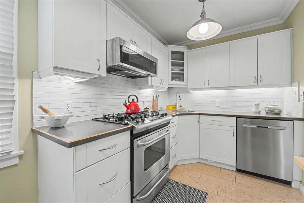 Bright white kitchen with stainless steel appliances, gray cabinets, and a red kettle on the stove.