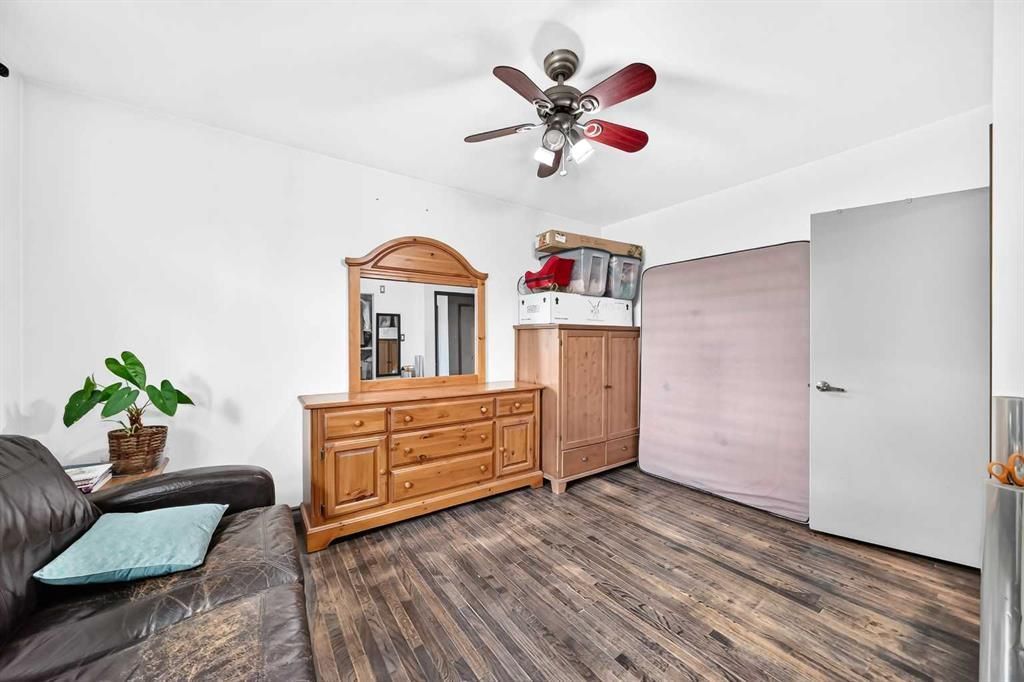 Bright bedroom with wood dresser, loft bed, gray sofa, and white closet on wood-look floor.