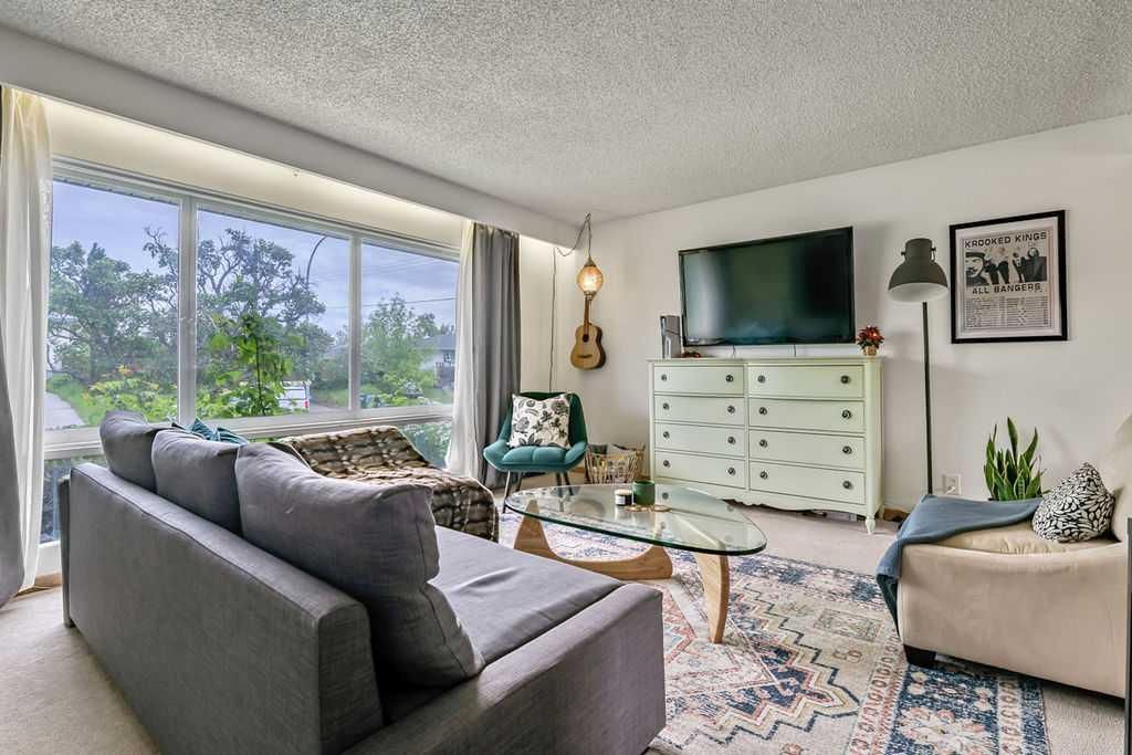 Bright living room with gray sofa, TV, dresser, armchair, and large window view