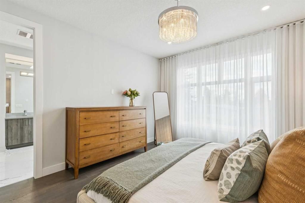 Bright bedroom with a wooden dresser, bed, chandelier, and floor-to-ceiling sheer curtains
