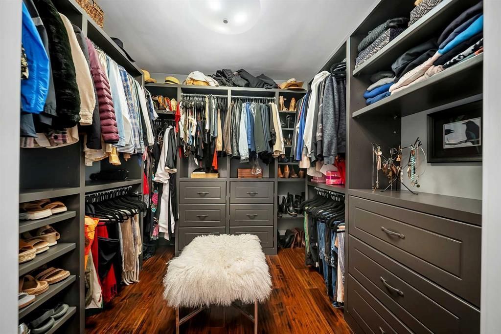 Walk-in closet with hanging clothes, drawers, and a white fluffy bench on wood flooring
