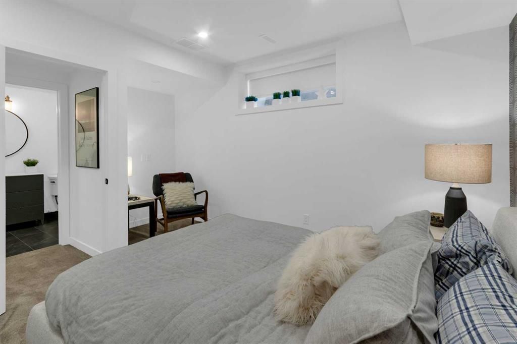 Bright bedroom with a bed, lamp, chair, and open bathroom door on the left.