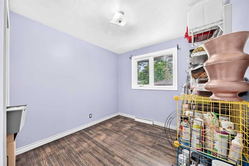 Empty lavender room with wood floor, window, and wire shelving with stacked items on the right