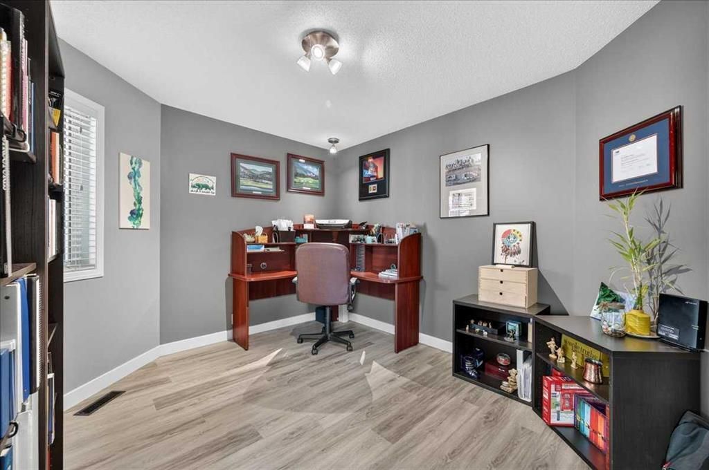 Small home office with desk, chair, framed art, and black shelving against gray walls