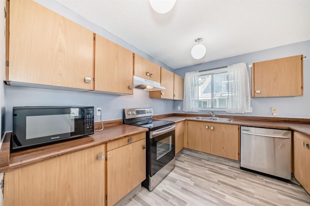 Compact kitchen with light wood cabinets, stainless steel appliances, and a window over the sink