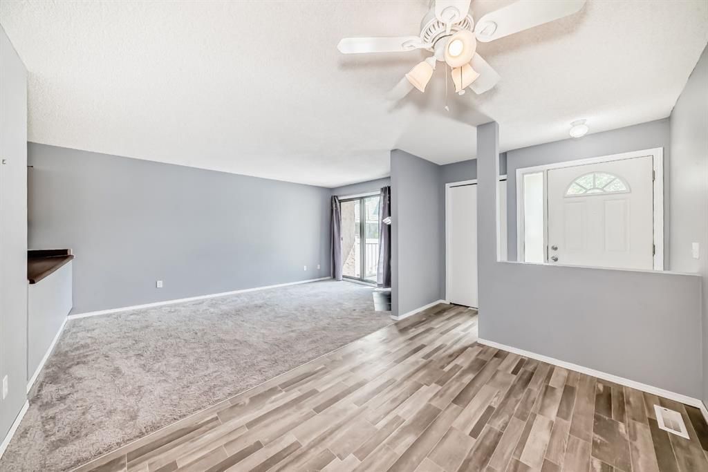 Empty living room with gray walls, wood-look flooring, carpeted area, and ceiling fan