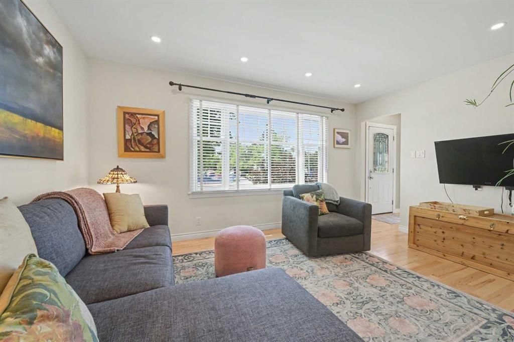 Bright living room with gray sectional, patterned rug, TV, wooden console, and large window.
