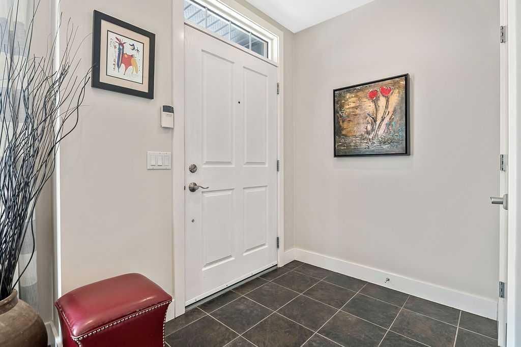 Small entryway with white front door, gray walls, tile floor, and framed wall art.