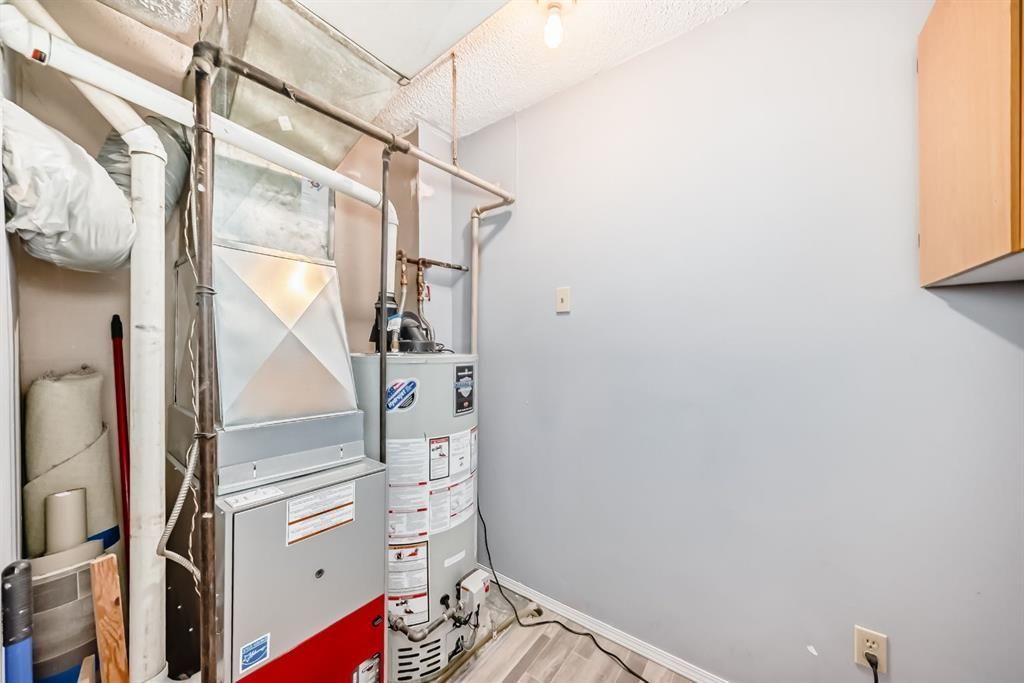 Utility closet with HVAC unit, water heater, exposed pipes, and shelving against white walls.