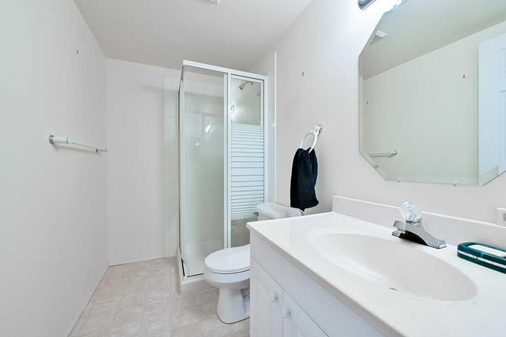 Bright white bathroom with shower, toilet, sink vanity, and large mirror.