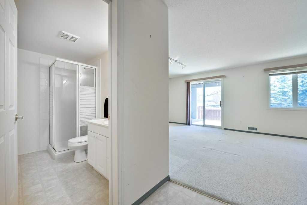 Bright empty living room with sliding glass doors and an adjacent bathroom hallway.