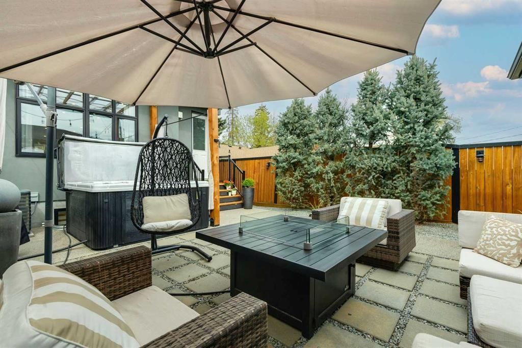 Outdoor patio with umbrella, wicker seating, and a fire table beside a house and wooden fence.