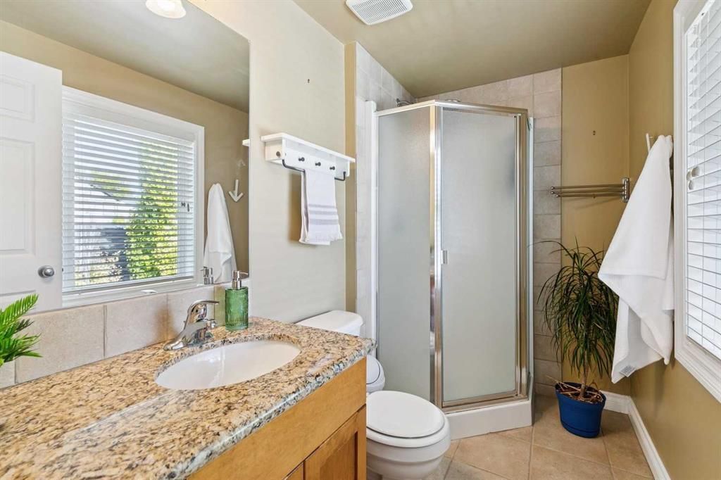 Bright beige bathroom with granite vanity, shower stall, toilet, and towels hanging on the wall