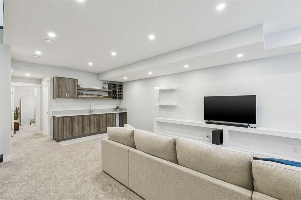 Bright modern open-plan living room with beige sofa, wall-mounted TV, and kitchen bar seating