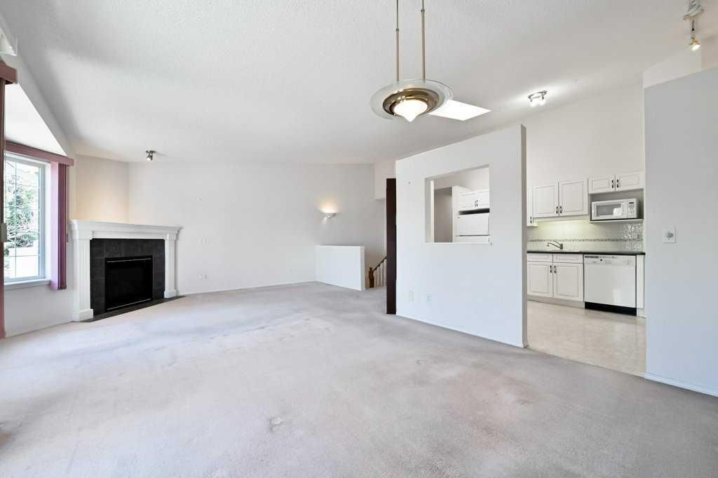 Bright empty living room with fireplace, white walls, ceiling fan, and open kitchen area
