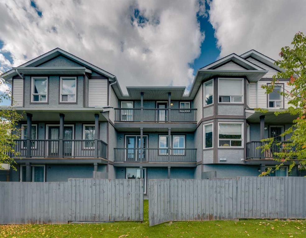 Blue-gray apartment building behind a tall white fence under cloudy sky