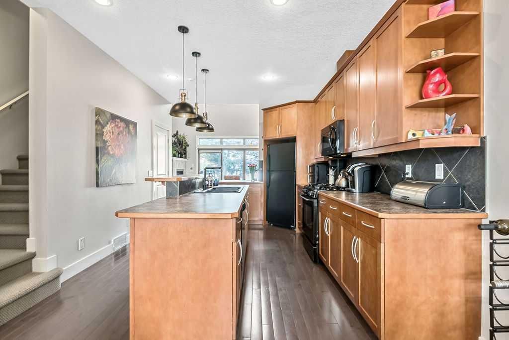 Modern kitchen with wood cabinets, black countertops, island, pendant lights, and stainless steel refrigerator