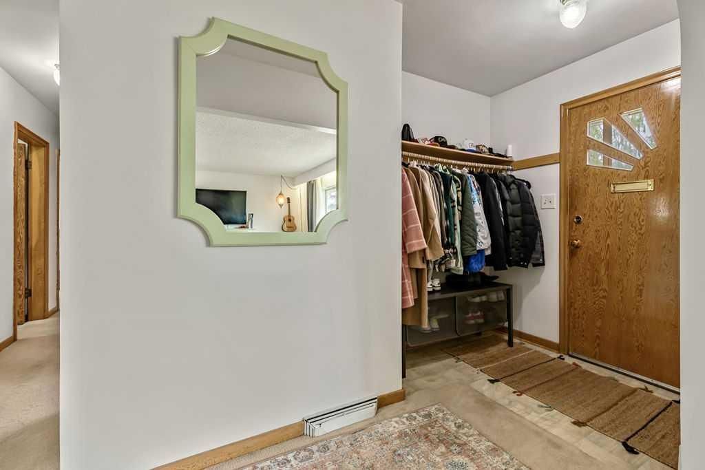 Front entryway with coat rack, wooden door, wall mirror, and small rug on tiled floor