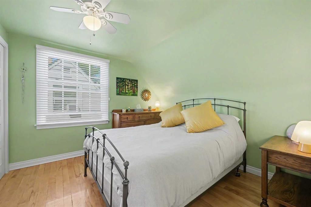 Small bedroom with light green walls, metal bed, yellow pillows, and a window with white blinds.
