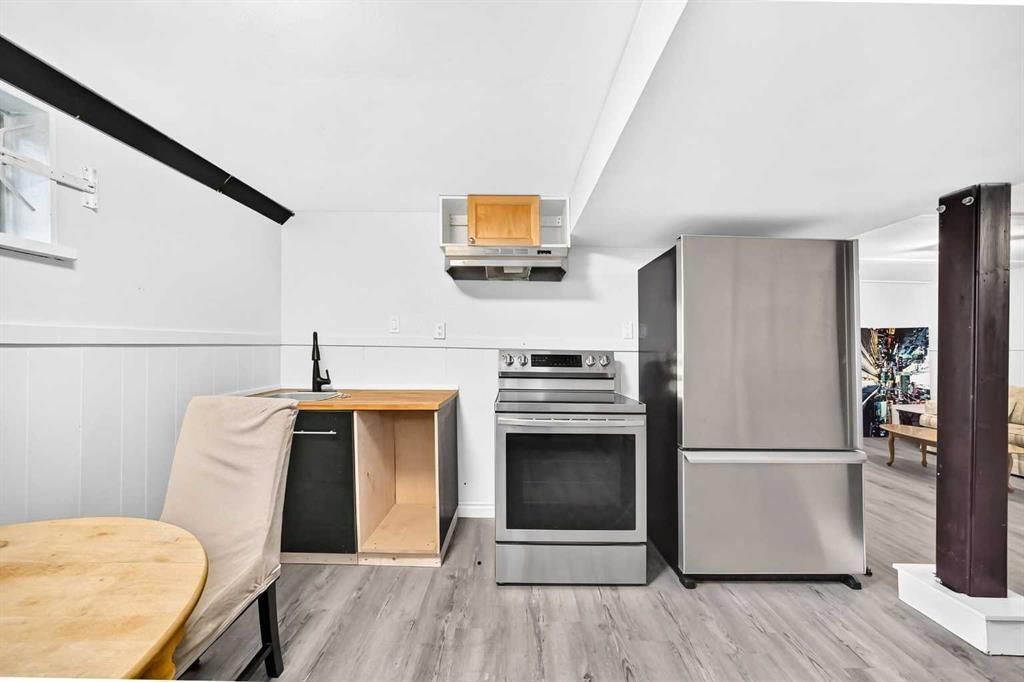 Small kitchen area with stove, refrigerator, cabinets, and a round table beside a bench seat.