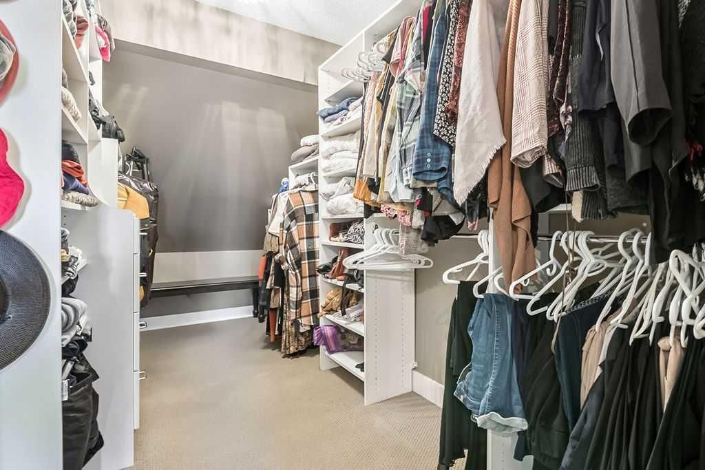 Narrow walk-in closet with clothes hanging on both sides and shelves, leading to a bright window at the back