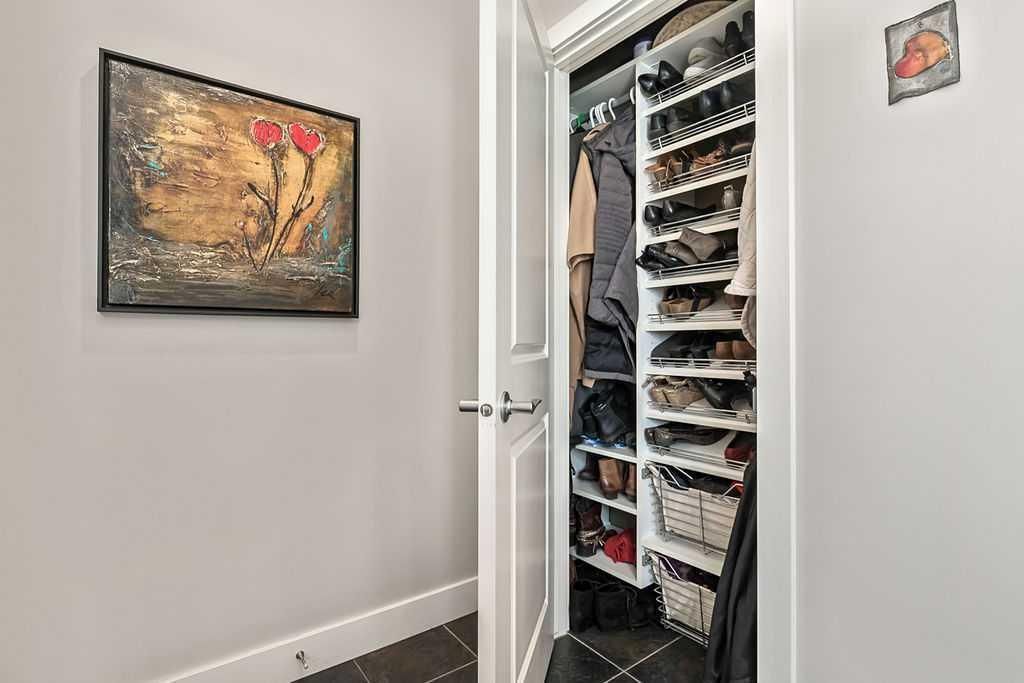 Hallway with an open closet packed with shoes and hanging clothes, beside a framed wall painting.