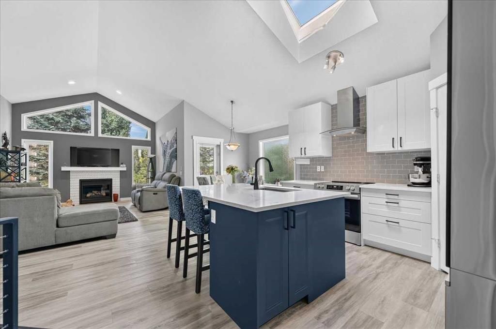 Bright open kitchen with navy island, white cabinets, and a living area with fireplace and large windows.