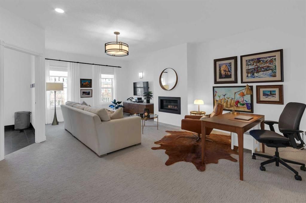 Bright living room with beige sofa, fireplace, desk, office chair, and framed art on white walls.