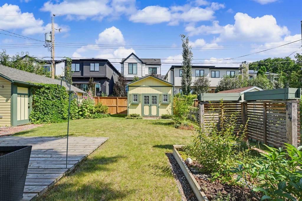 Backyard garden with lawn, raised beds, and a small shed under a blue sky, with houses in the background