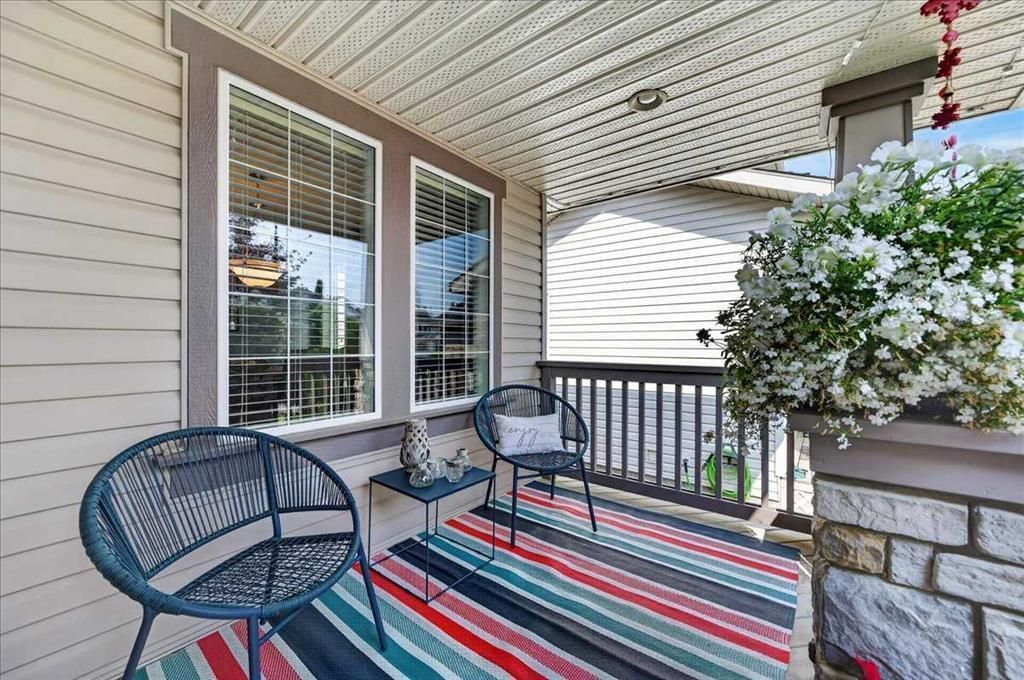 Covered porch with blue chairs, striped rug, and white flowers beside a stone planter.