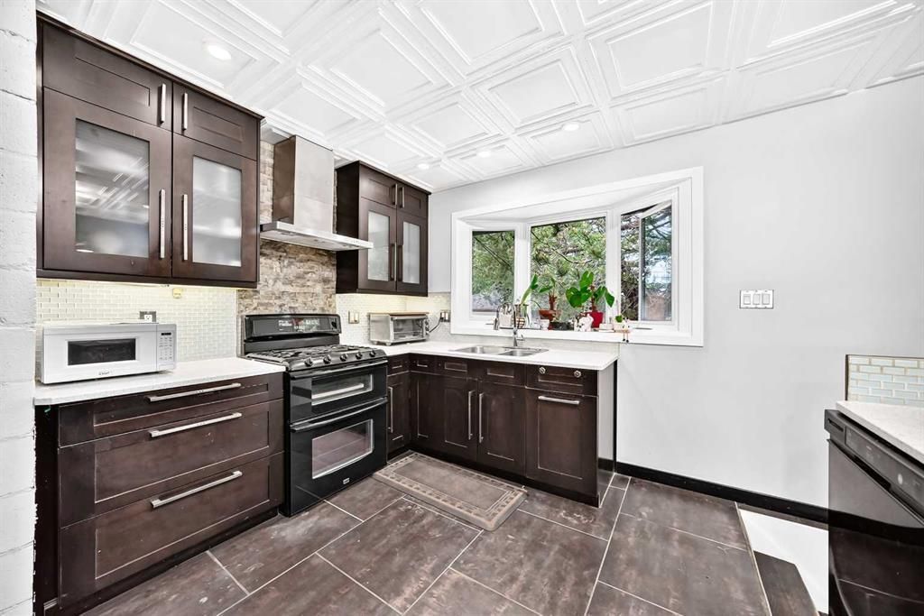 Bright kitchen with dark wood cabinets, black stove, white countertops, and a window above the sink