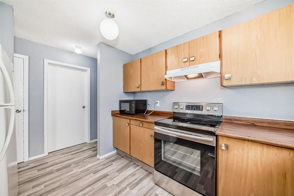 Small kitchen with light wood cabinets, black stove, white refrigerator, and gray wood-pattern flooring.