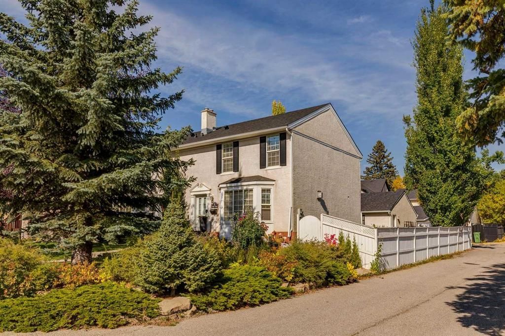 Suburban house with white fence, garden, and tall trees along a quiet street