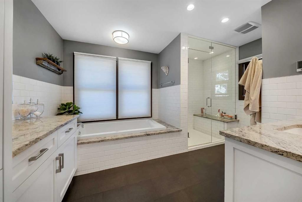 Bright modern bathroom with double vanity, glass shower, soaking tub, and large frosted window.