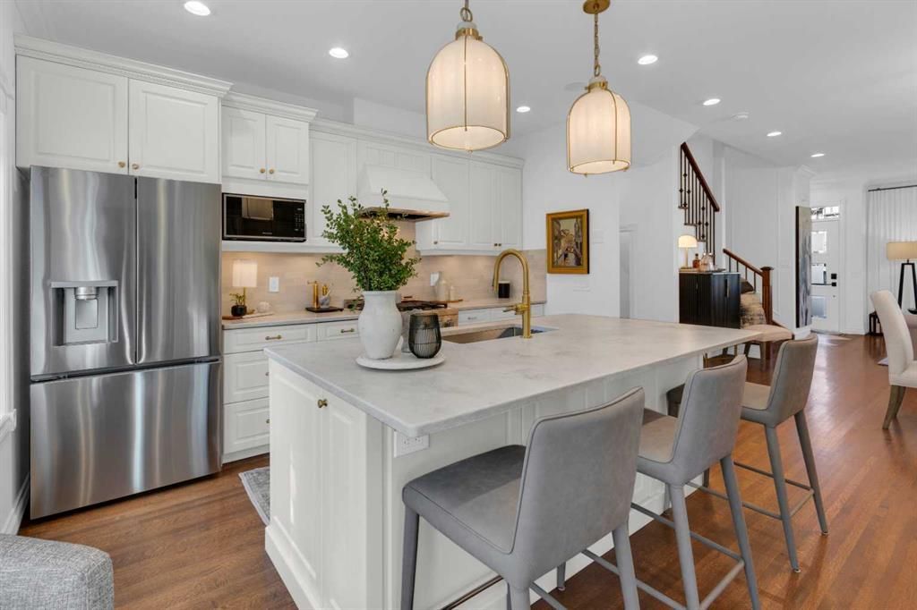 Bright white kitchen with stainless steel fridge, large island, pendant lights, and bar stools