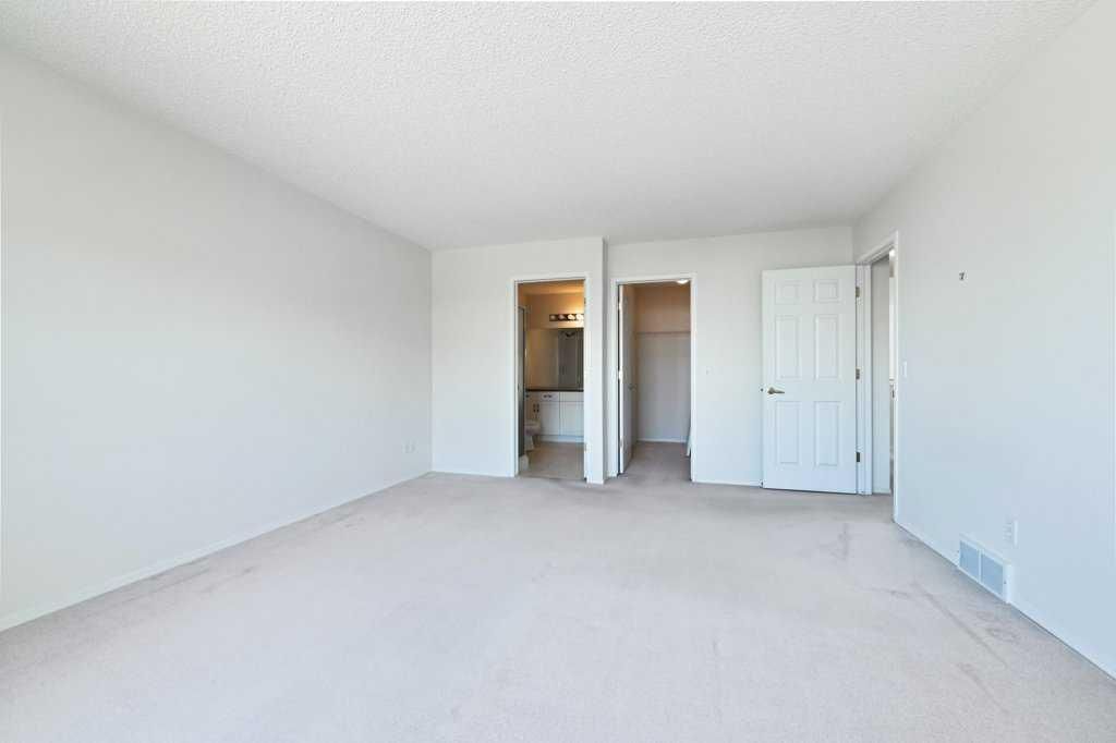 Empty white bedroom with carpet, open closet, and bathroom doorway