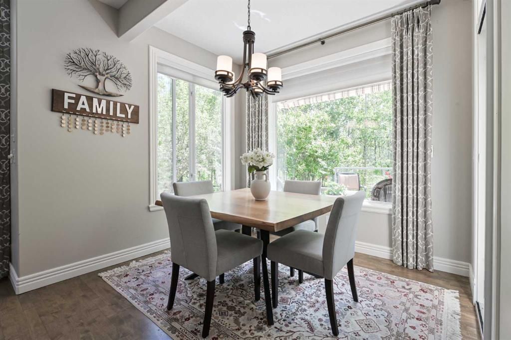 Dining room with wooden table, gray chairs, chandelier, and large windows with curtains.