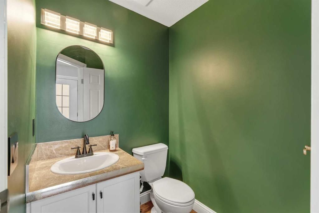 Small bathroom with green walls, a white toilet, and a vanity with sink and oval mirror.