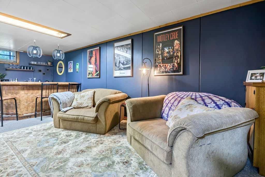 Blue-walled basement lounge with two tan sofas, shag rug, bar stools, and movie posters