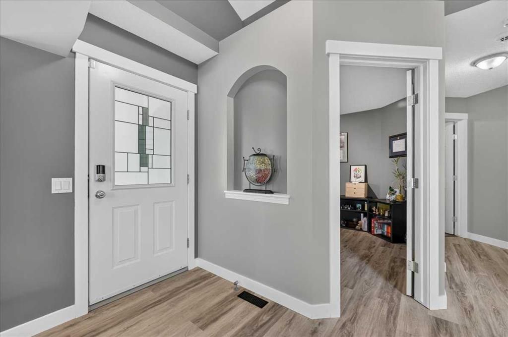 Modern entryway with white front door, gray walls, wood floors, and open doorway to a room.