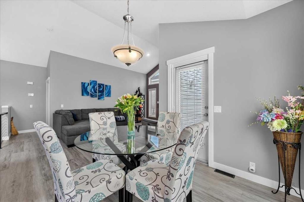 Modern dining room with glass table, patterned chairs, gray walls, and floral arrangements.