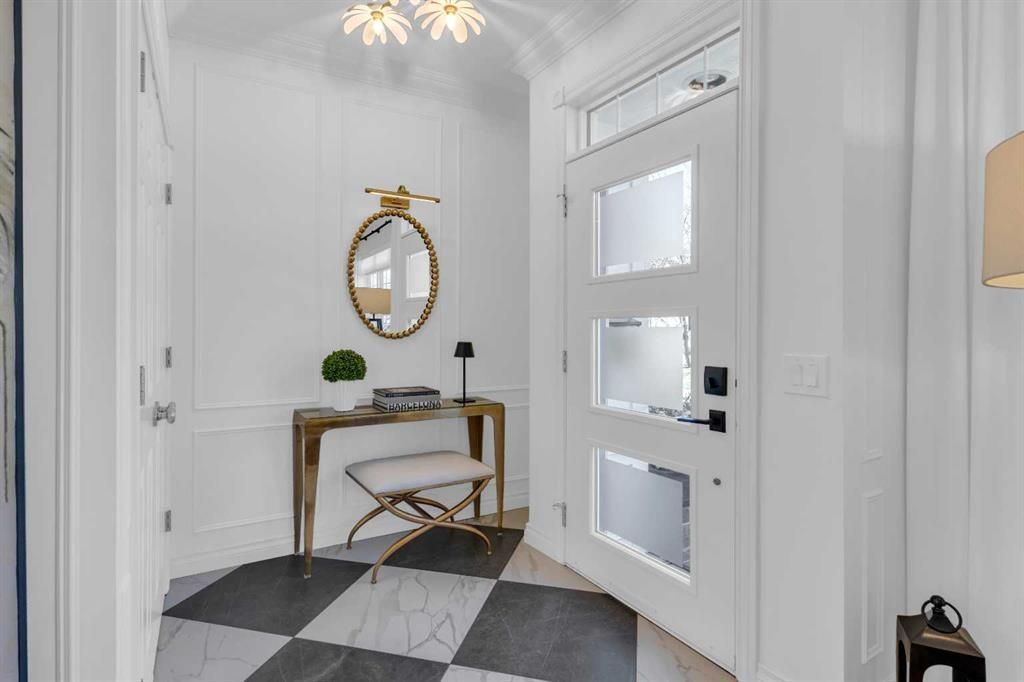 Bright white entryway with black-and-white tiled floor, gold mirror, console table, and front door
