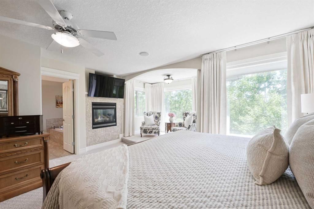 Bright bedroom with a large bed, fireplace, ceiling fan, and windows with white curtains