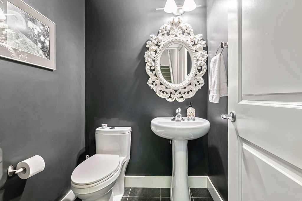 Small bathroom with toilet, pedestal sink, ornate mirror, and gray walls