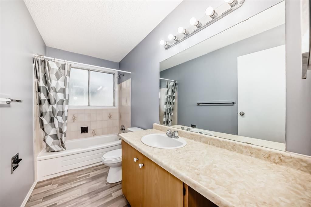 Bright bathroom with double vanity, large mirror, tub, and window with patterned curtains.