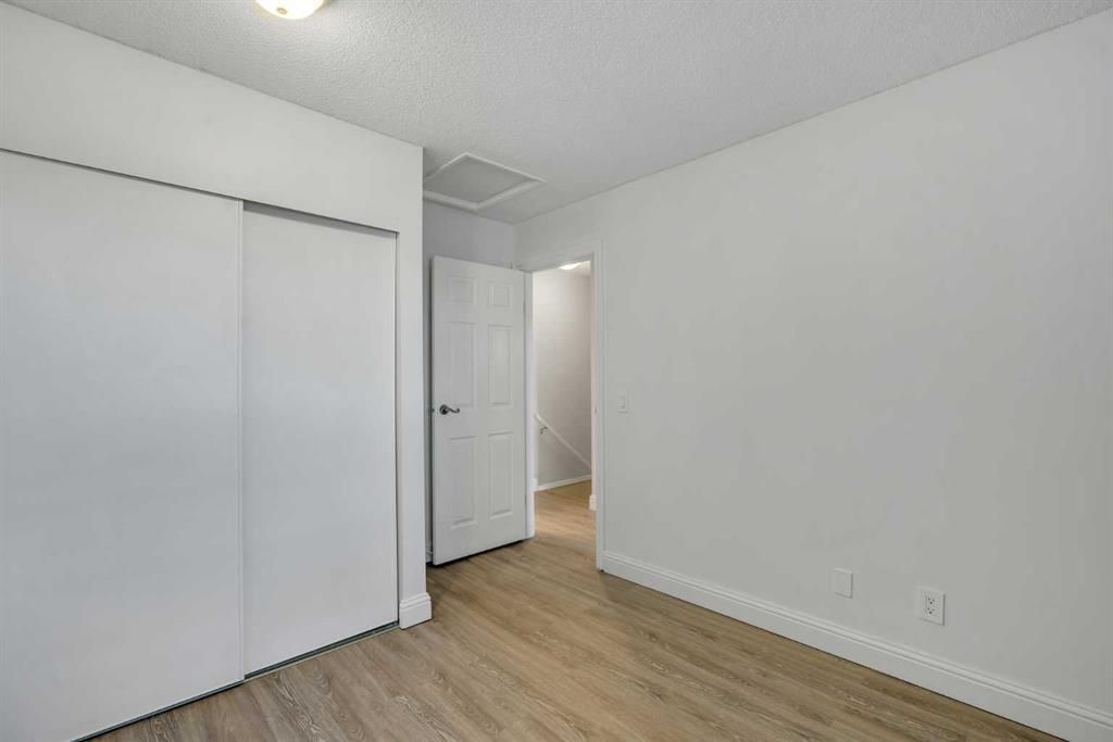 Empty white bedroom with sliding closet doors and wood flooring, viewed from the doorway